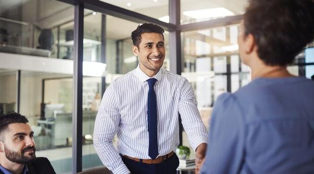 Two colleagues seated at a table engaging in conversation with a colleague standing nearby